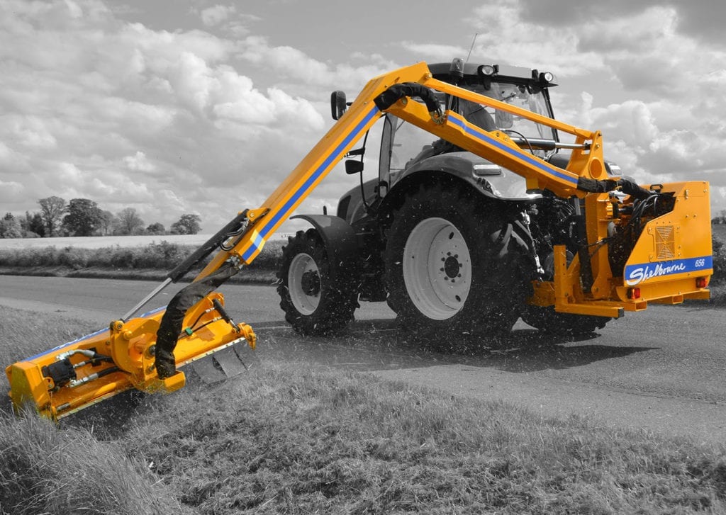 A yellow Shelbourne Reynolds tractor with a blade on the side of the road.