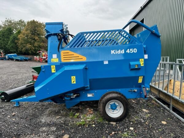 A blue baler, the Kidd 450 bale shredder, is parked in front of a building.