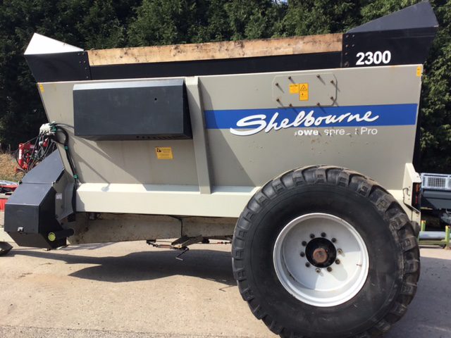 A Shelbourne muck spreader with a large wheel on it.