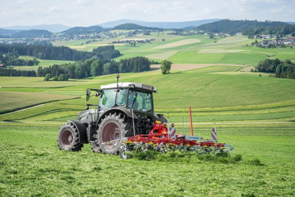 A tractor equipped with the POTTINGER HIT 6.61 TEDDER plowing a field in the countryside.