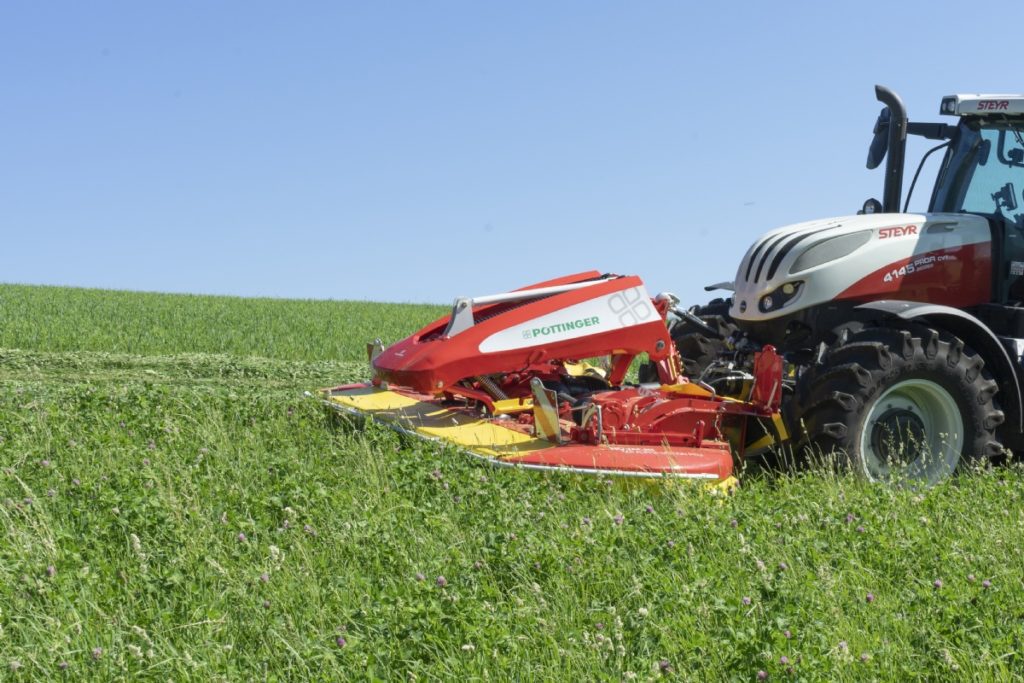 A red and white POTTINGER NOVACAT 301 ALPHA MOTION PRO ED mower in the middle of a green field.