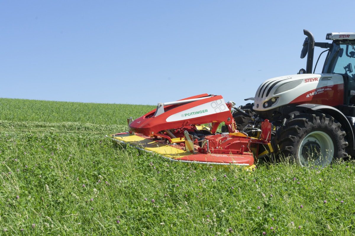 A red and white POTTINGER NOVACAT 301 ALPHA MOTION PRO ED mower in the middle of a green field.