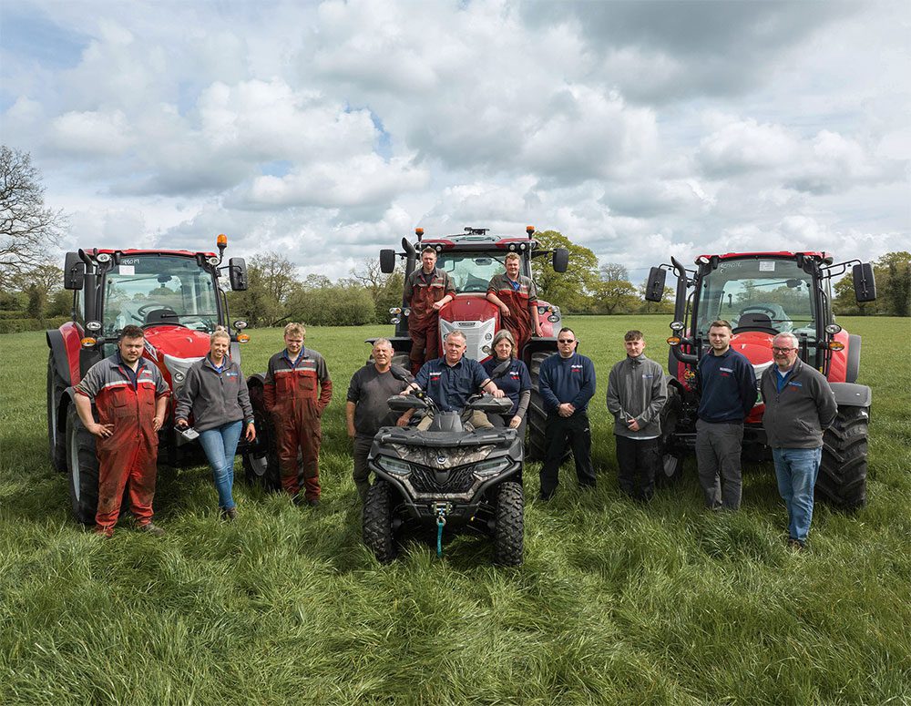 A group of people posing with tractors in the field.