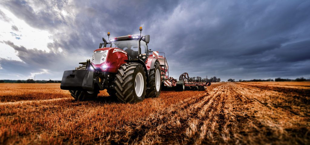 A red tractor in a field under a stormy sky.